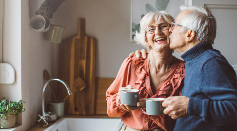 Senior couple for Christmas at home. They are standing in front of kitchen window and drinking tea or coffee.